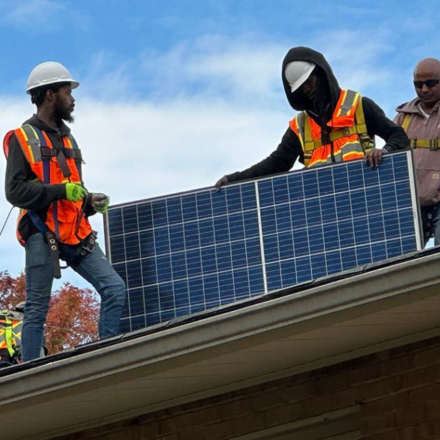 Three men installing a solar panel on a roof.