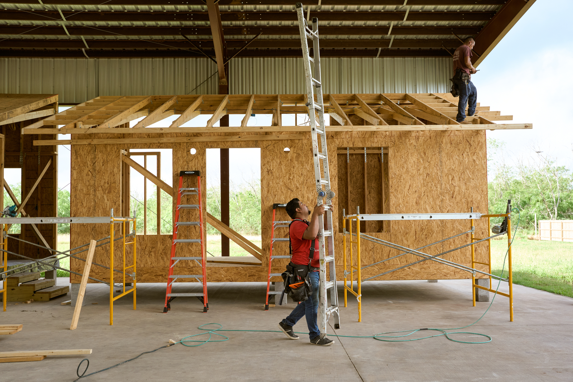 Construction worker carries a ladder in front of a home being built