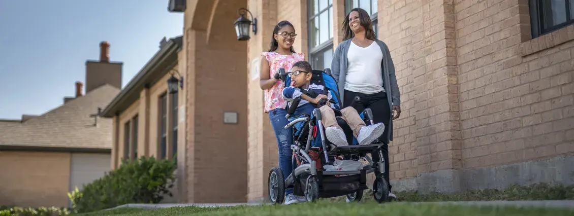 Two women, and a young man in a wheelchair out for a walk in front of a building