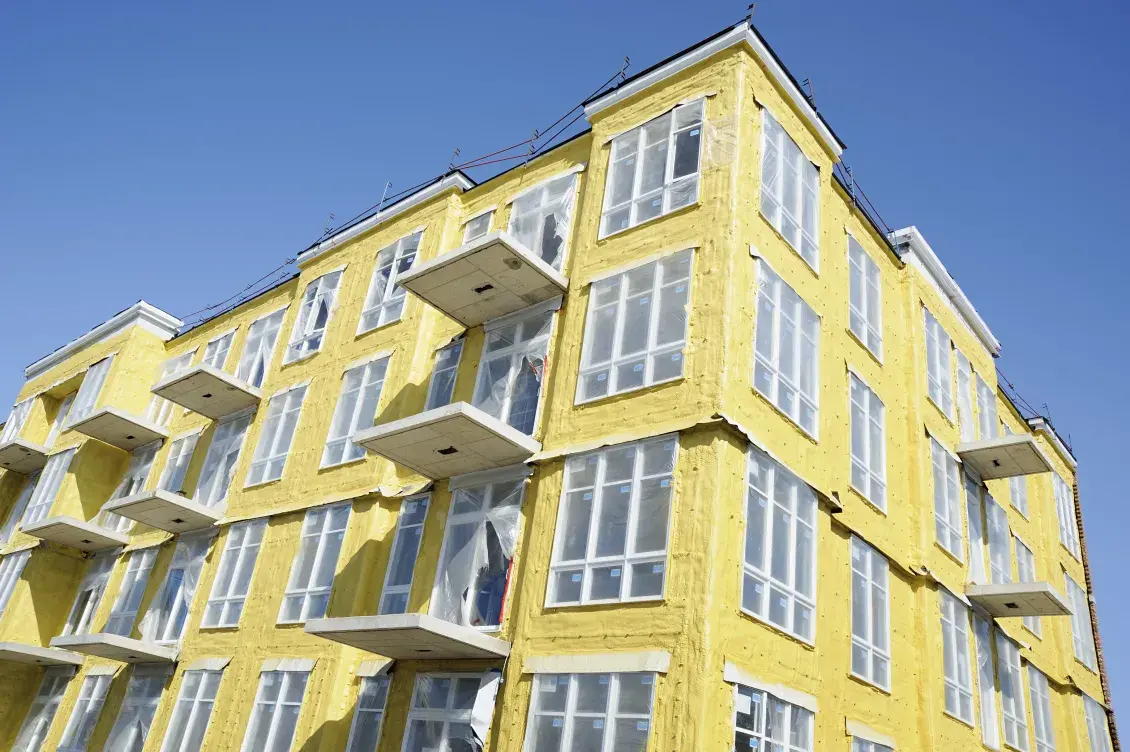 Aspect of a multistory building with yellow insulation and a bright blue sky overhead.
