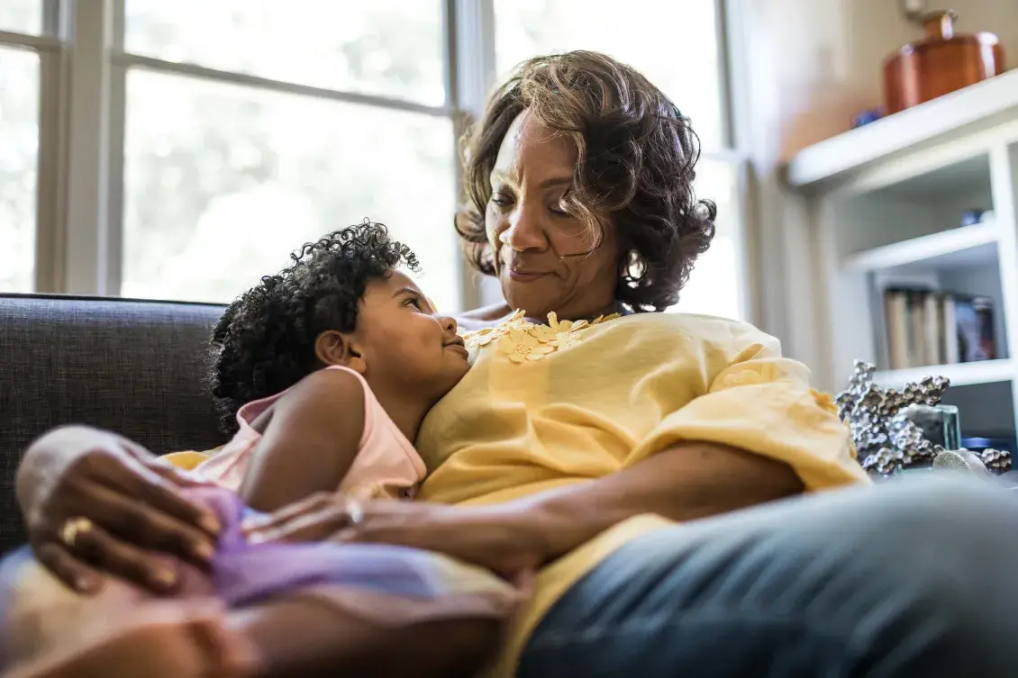 Girl and grandmother look at each other as they sit together on a couch