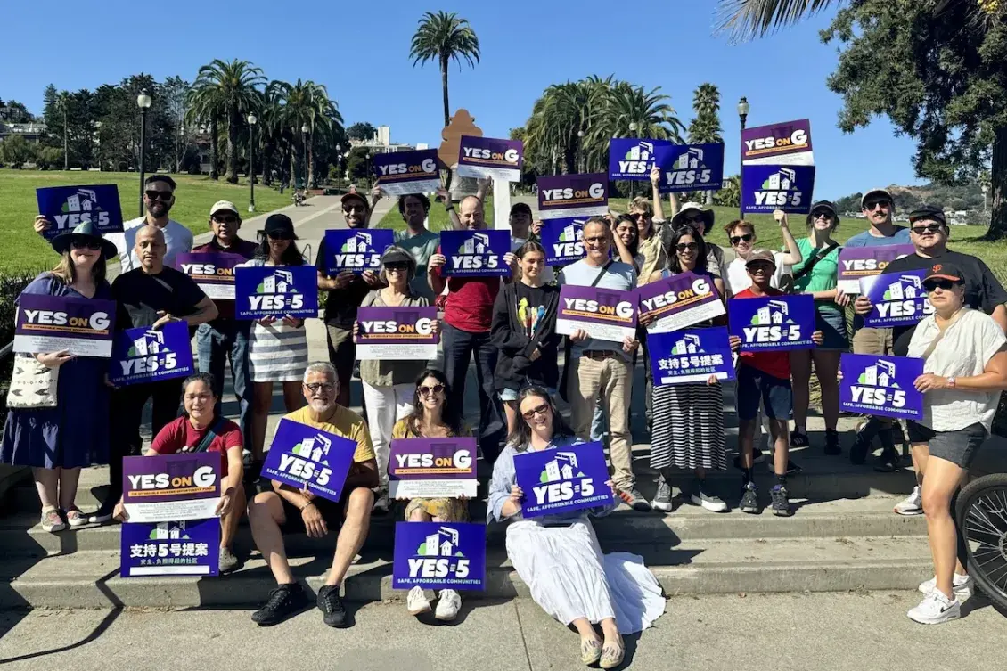 A group of people holding blue, Yes on Prop 5 signs in front of a park setting