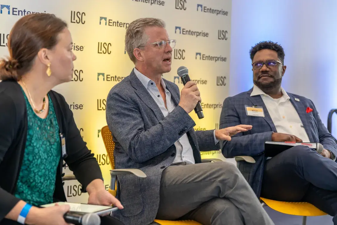 Three people sit in a row engaged in conversation with the center person holding a mico