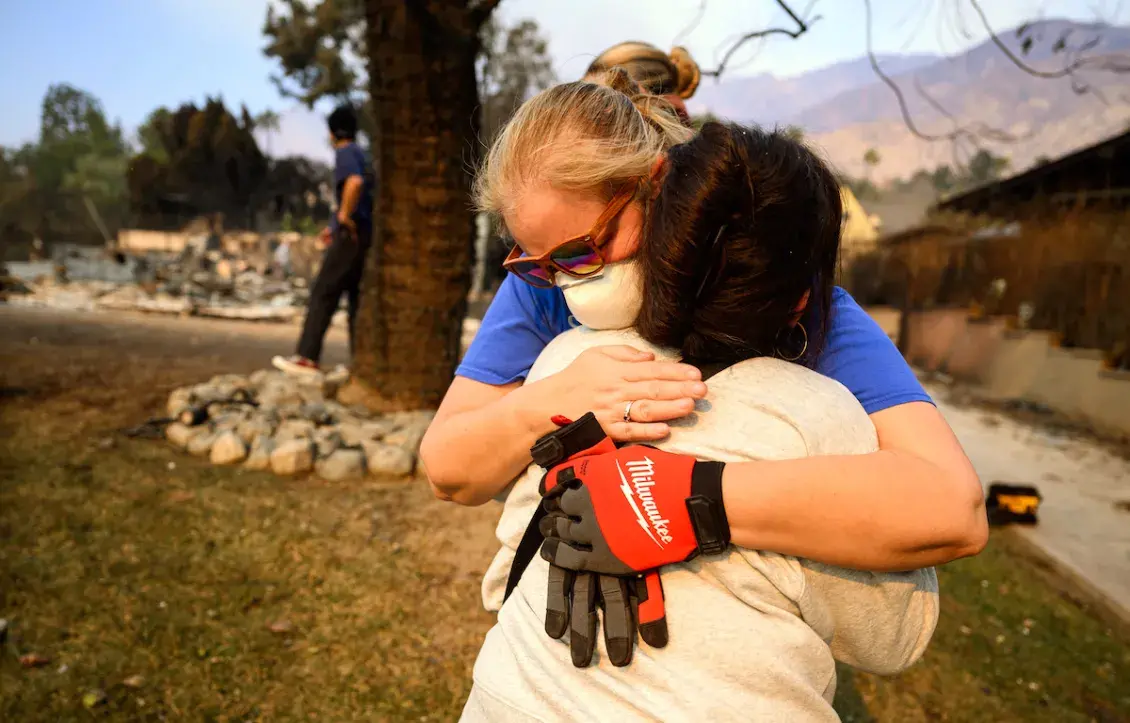 Two women hugging in their neighborhood devastated by wildfires