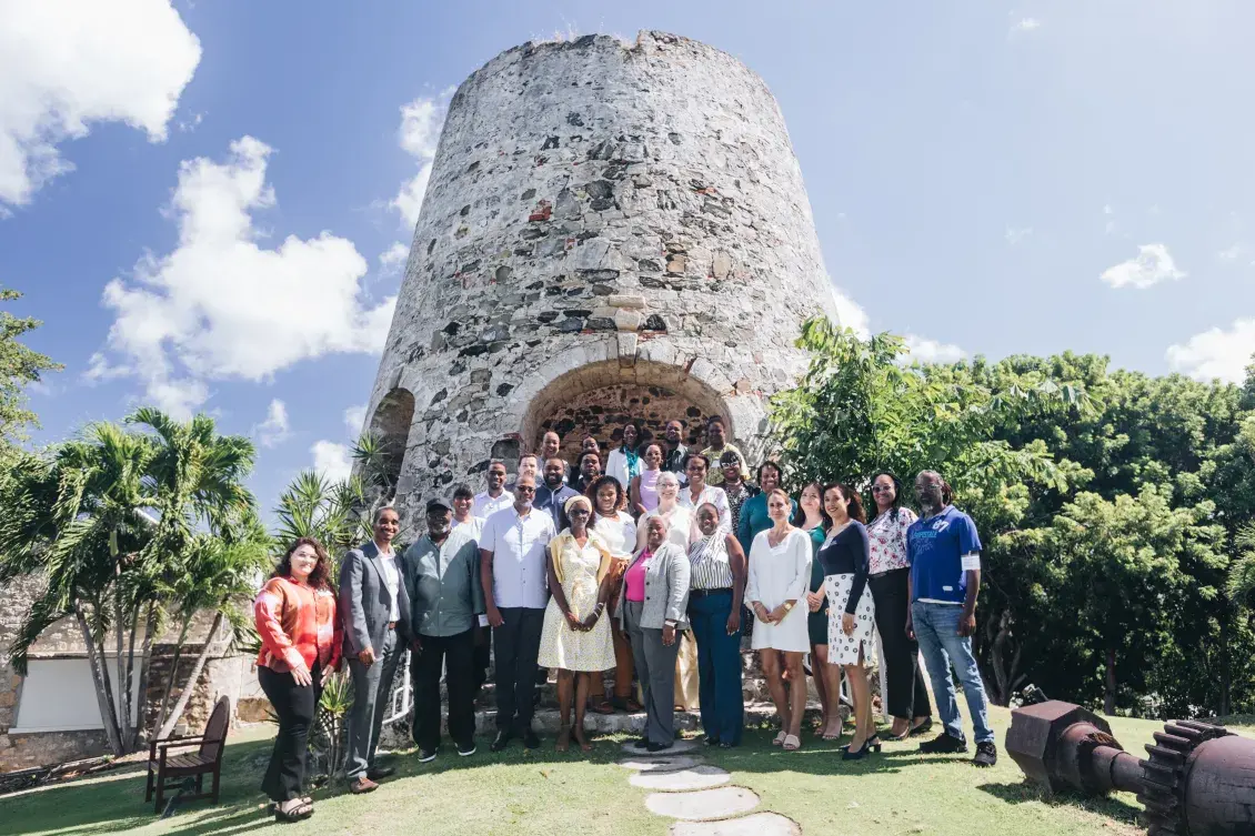 Attendees at the Housing Our Community Workshop in St. Croix, USVI stand in front of a historic structure with trees beside it