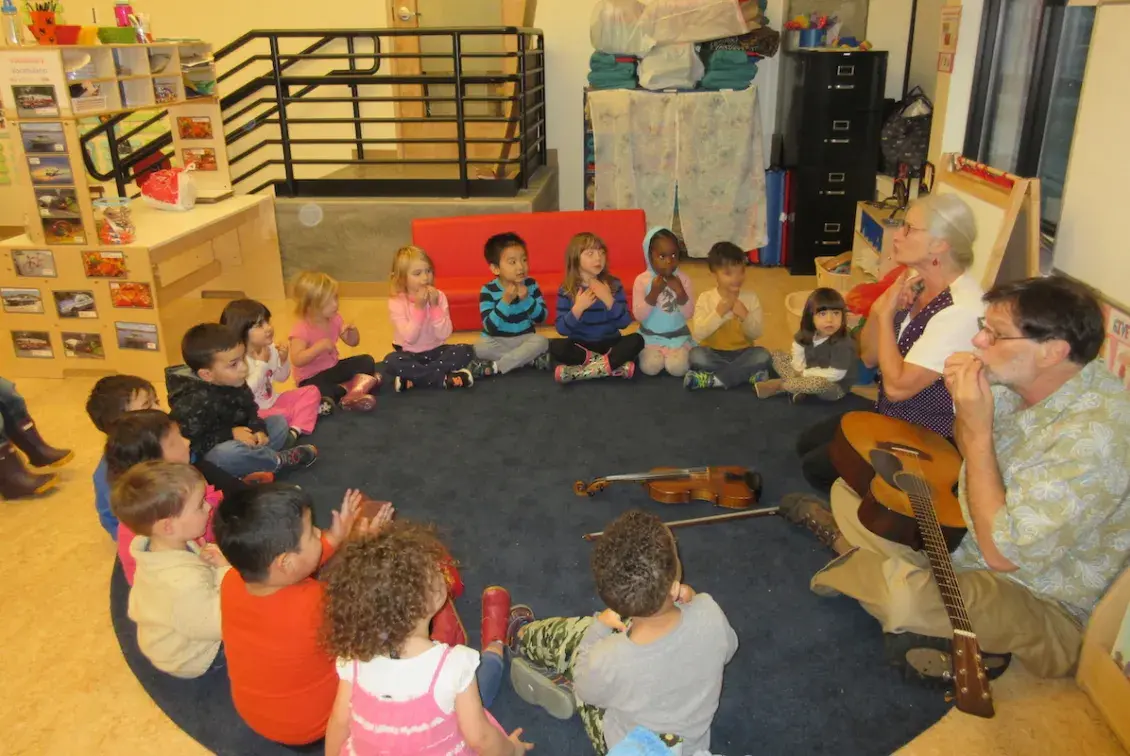 Children sitting on the floor in a circle participating in a music lesson
