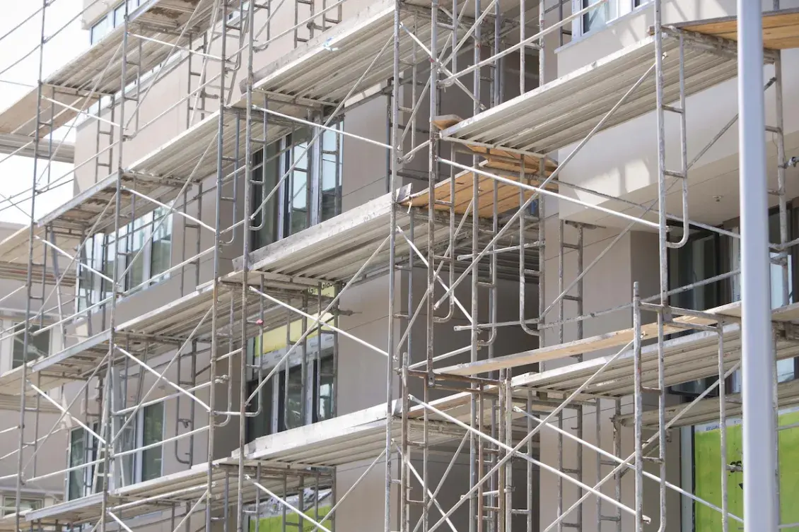 Scaffolding surrounds a multi-story residential building under construction, with partially installed windows and exterior finishes visible.