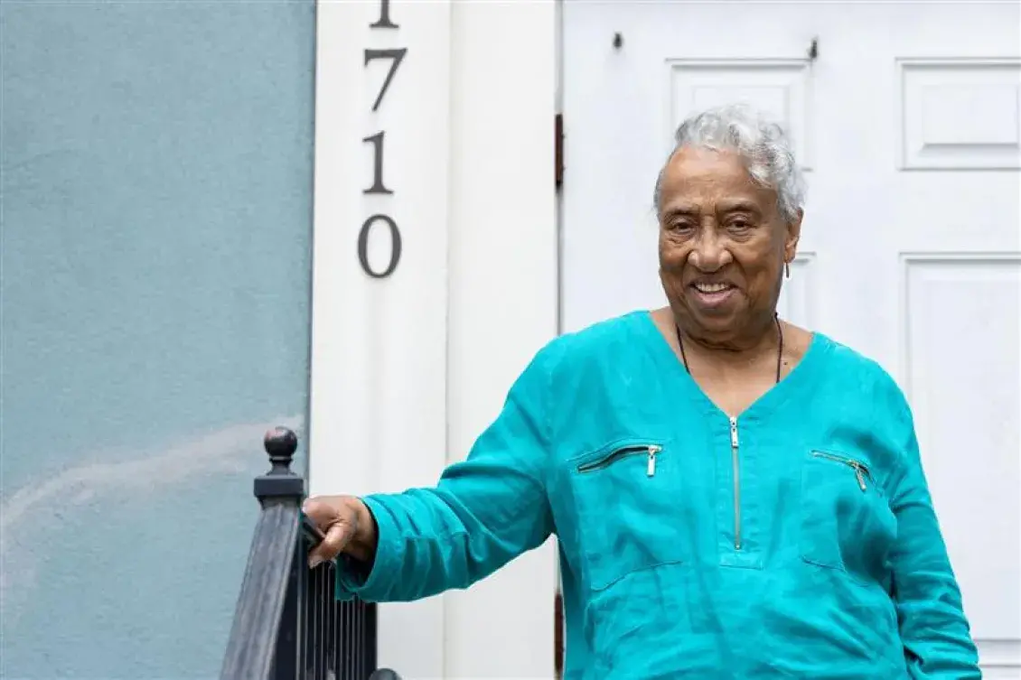 Emelda Paul stands on the steps of her front door with her hand on the railing