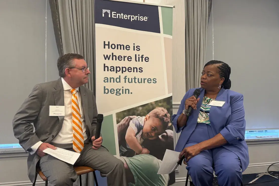 Woman in blue suit interviewing man in grey suit and striped, orange tie.