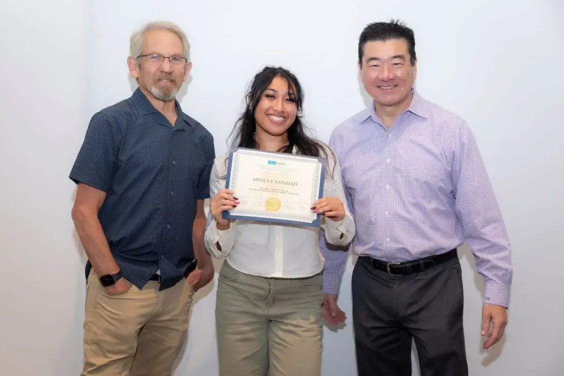 A woman standing between two men holding up a professional certificate