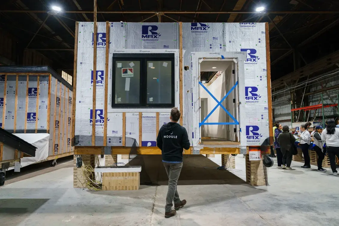 Person stands in front of modular housing in factory setting