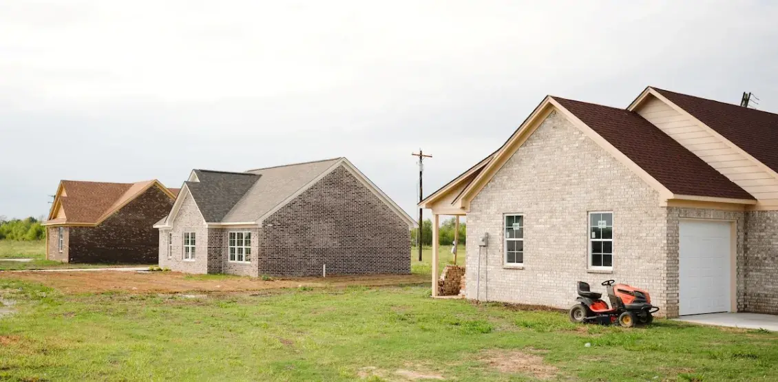 Three light colored brick homes with a riding lawn mower next to one