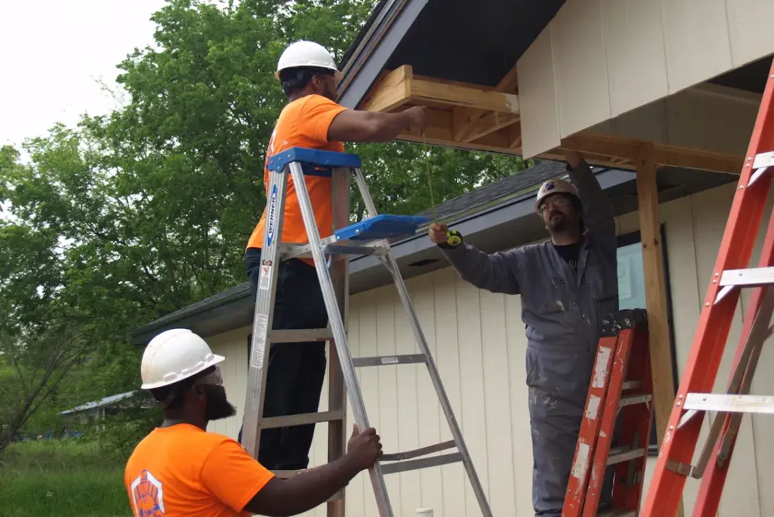 Men in orange clothing on ladders working on building