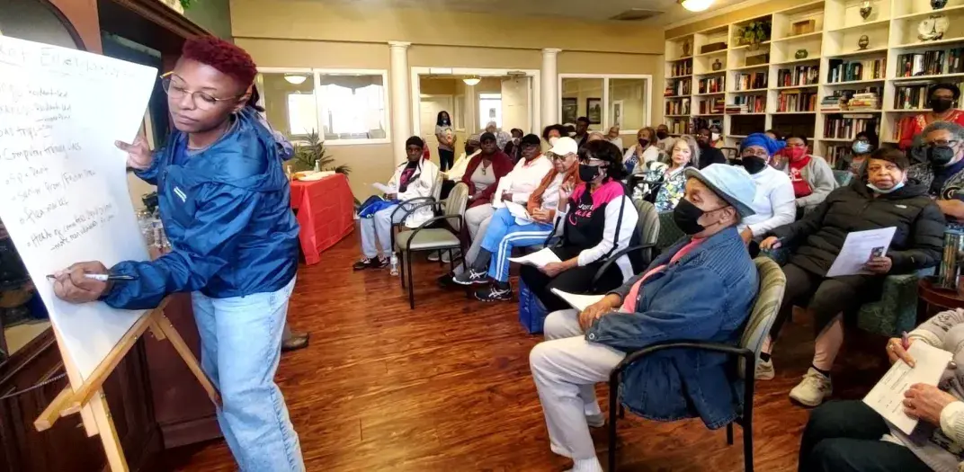 An instructor writes on easel paper in front of a room of people sitting in chairs