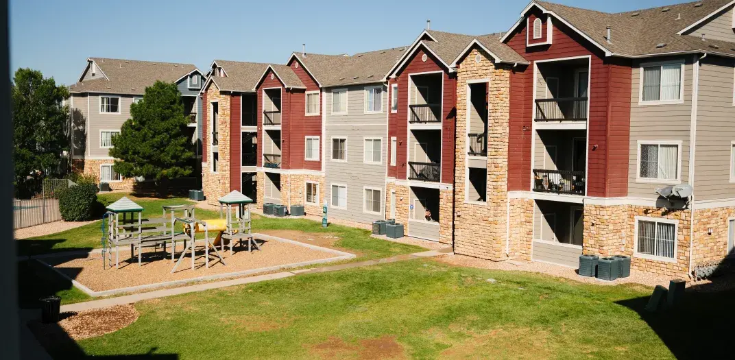 A row of apartment buildings and a playground with a grassy area
