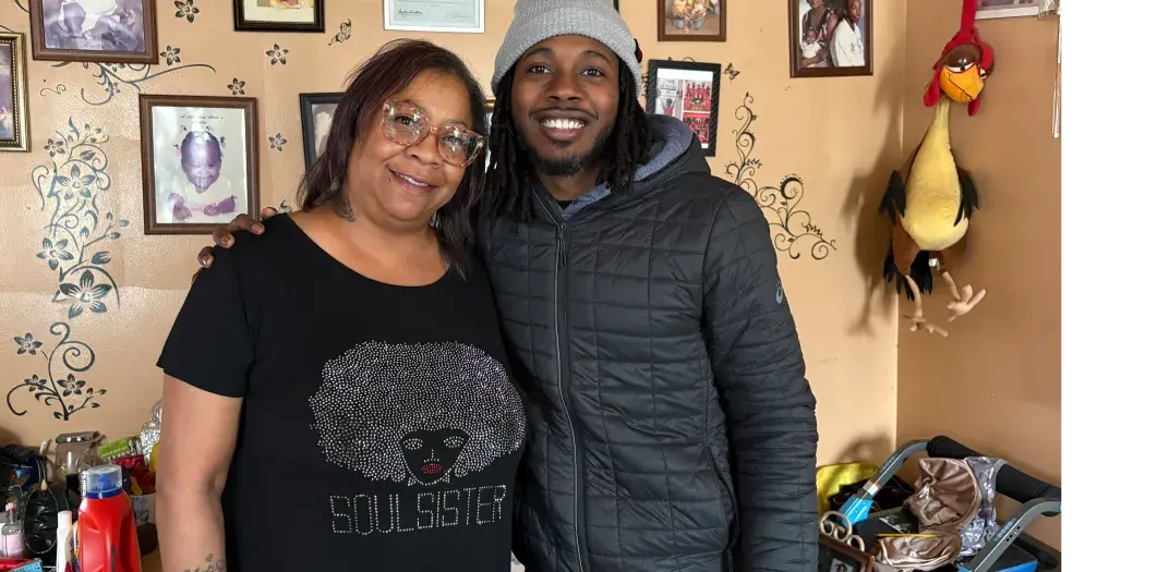 A mother and her son stand in front of a wall of pictures and decorations
