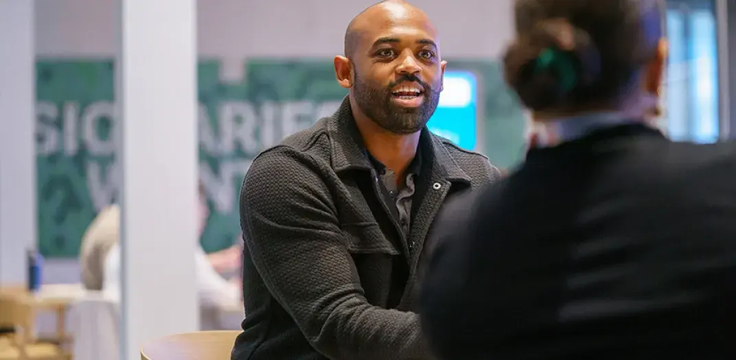 A man in a black jacket sitting and talking a woman across a table.