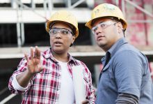 Two workers in hard hats discussing a project on a building site.