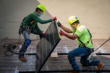 Two solar panel installers hold a solar panel to install on a rooftop