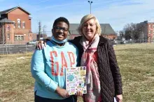 A young mentee and mentor stand at a park with apartment buildings in the background 