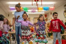 Children in brightly colored clothing dancing in classroom.