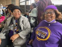 Two people sit next to each other, each wearing a purple hat, and T-shirts with the words "Brightmoor Seniors a Go Go."