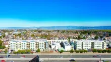 Large white apartment building with freeway in foreground and mountains in background