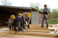 Three construction workers teach a teenager how to do carpentry work. 