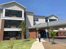 A woman entering the new development with a covered roundabout driveway and state of the art new homes with lush balconies.