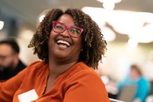 A woman wearing an orange shirt and red glasses smiling