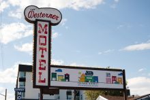 A sign in front of a building that reads "The Westerner Motel" and notes that the area is a cultural district; a blue sky with white clouds is in the background 