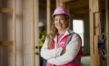 A person wearing a hard hat and standing with their arms folded