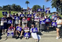 A group of people holding blue, Yes on Prop 5 signs in front of a park setting