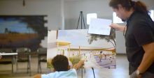 Child points to a spot on a drawing on an easel with an adult standing and looking at the drawing