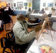 Older man in wheelchair painting on a small canvas and easel.