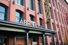 Exterior of red brick building with tall arched windows and a sign that reads "Fábrica Lofts"