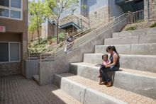 Mother and child sit reading on the stairs of a housing development