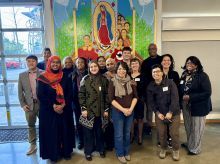 Group of smiling people standing in front of colorful mural