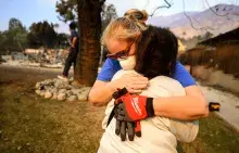 Two women hugging in their neighborhood devastated by wildfires