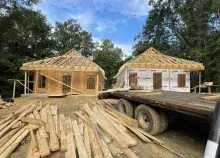 Two homes under construction stand side by side with a blue sky and treetops in the background