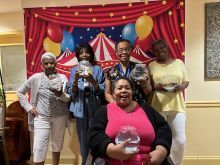 A group of women hold goldfish bowls in front of a wall with circus-themed wallpaper