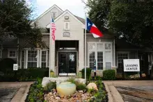 An apartment leasing center modeled as a home with trees on both sides and flags in the front
