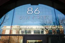 Closeup of 86 Otis Street Putnam School Apartments in white on the arched glass with a reflection of a building