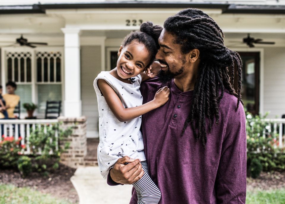 Father holds his daughter in front of their home