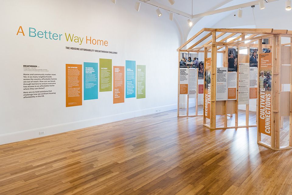 An exhibit room of a wooden structure and the words A Better Home Way Home on the wall 