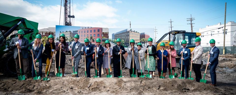 A group of people lined up with green shovels and hard hats for a groundbreaking