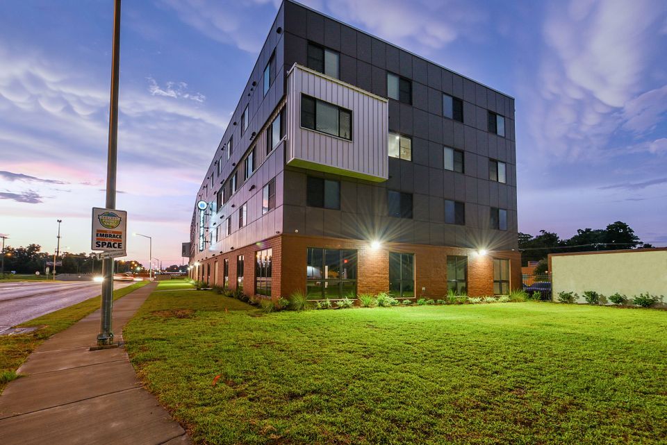 Dramatically lit modern looking multi-story housing development with a blue sky in the background and vibrant green grass in the foreground.