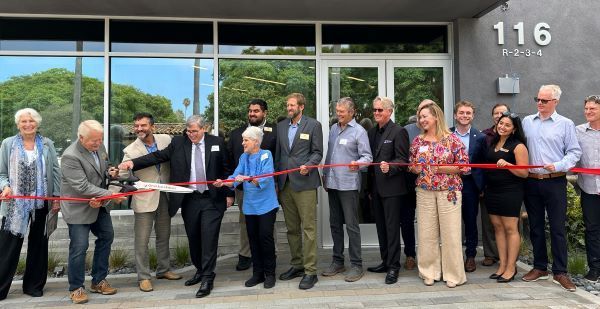 A man cutting a ribbon at an outdoor event, with a group of people behind him.