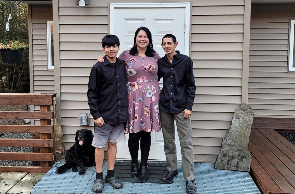 A mother with her two sons standing in front of their home