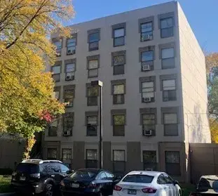 Apartment building with cars parked in front and a tree with yellow leaves